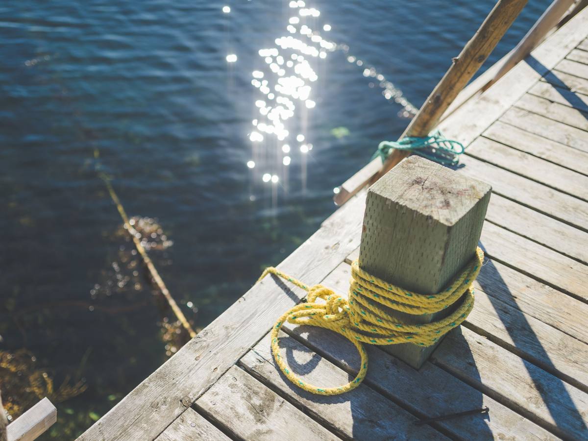 Yellow rope coiled around a wooden post on a weathered dock above sunlit water