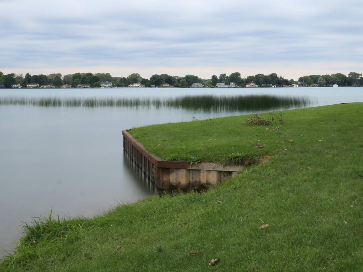 Bulkhead corner holding a green lawn at the water's edge, with waterfront homes across the water