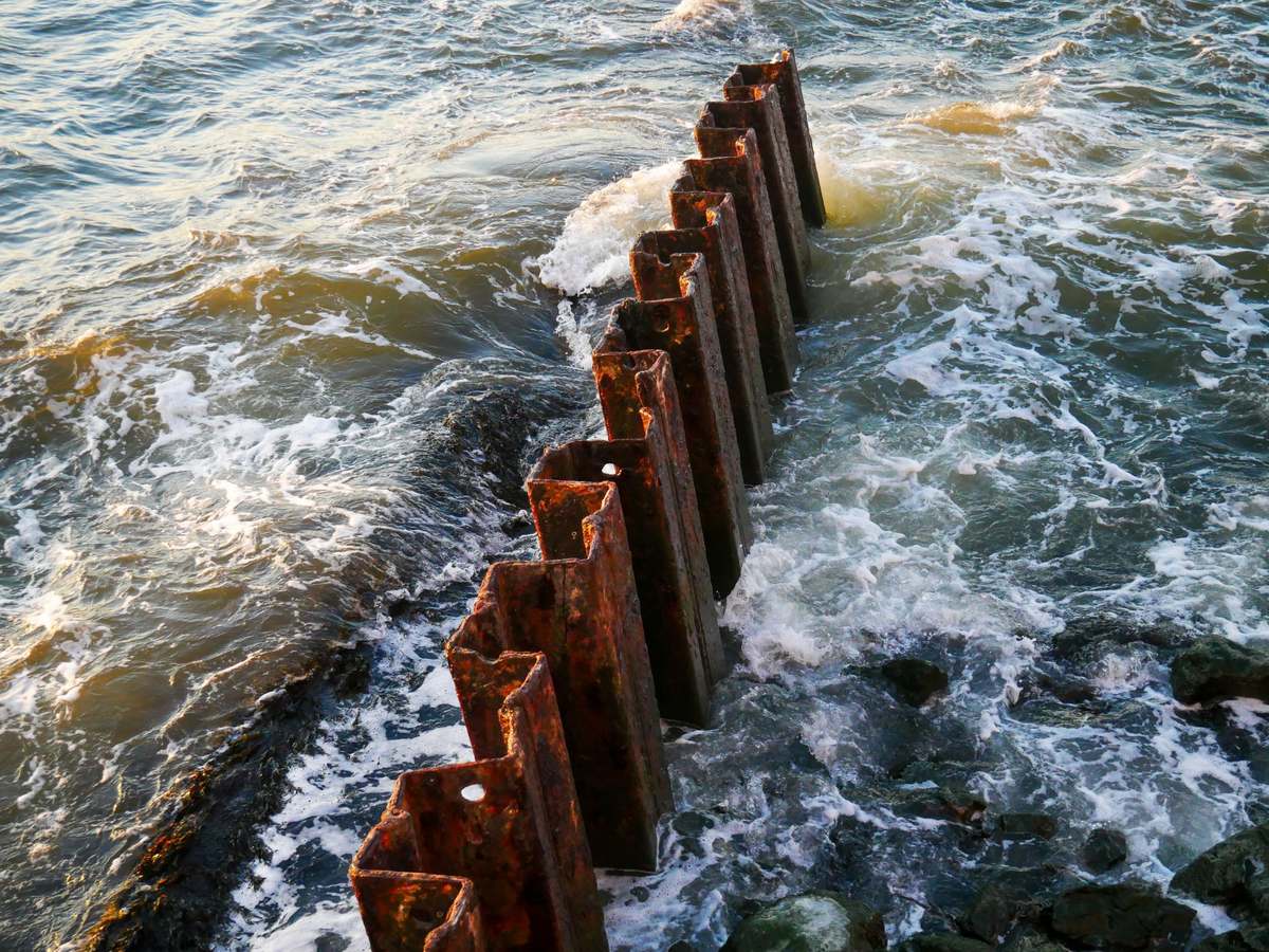 Rusted steel sheet piling in choppy salt water, showing how bare steel corrodes over time