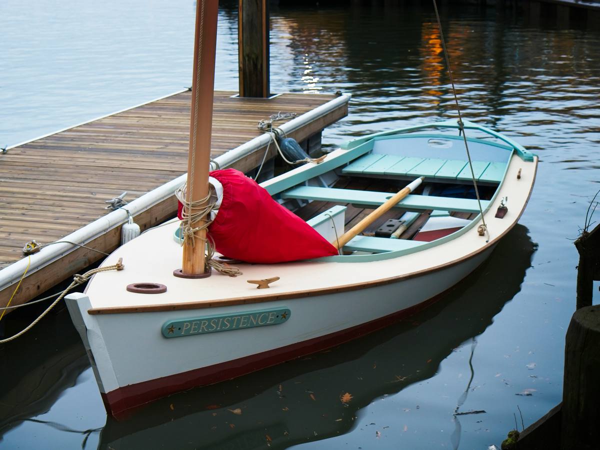 Wooden sailing skiff with a red sail cover tied to a floating dock