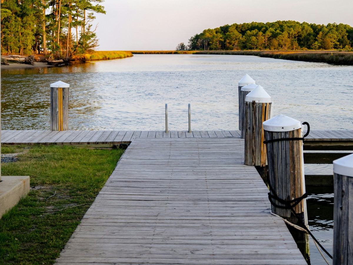 Wooden dock with capped pilings on a tidal creek lined with marsh and pine trees