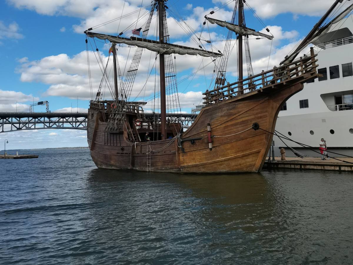 Wooden sailing ship docked at the Yorktown waterfront on the York River, with the Coleman Bridge behind